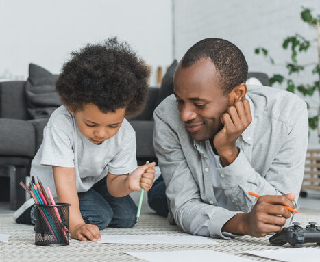 african american father drawing with son and mother reading book at home