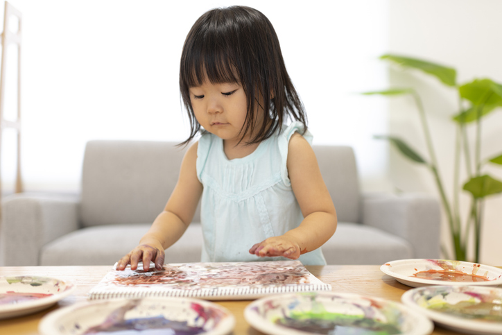 A girl puts paint on her hand and draws a picture